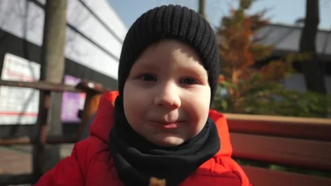 A little boy in a red jacket sits on a bench and eats baby food Stock Footage 270679506