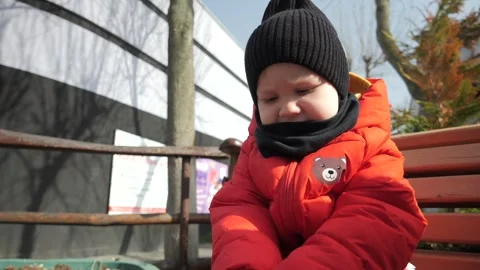 A little boy in a red jacket sits on a bench and treats his hands with antisepti Stock Footage 270679799