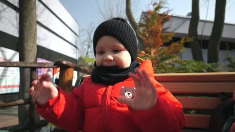 A little boy in a red jacket sits on a bench in the park and dries his hands aft Stock Footage 270679815
