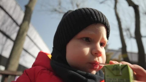  A little boy in a red jacket sits on a bench in the park and drinks juice Stock Footage 270679824
