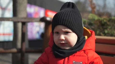 A little boy in a red jacket sits on a bench and eats baby food Stock Footage 270889478