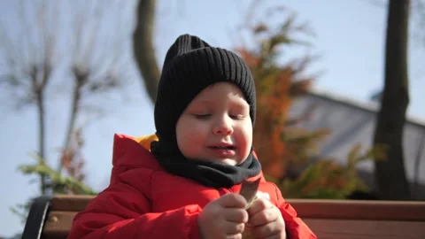 A little boy in a red jacket sits on a bench and eats baby food Stock Footage 270889608