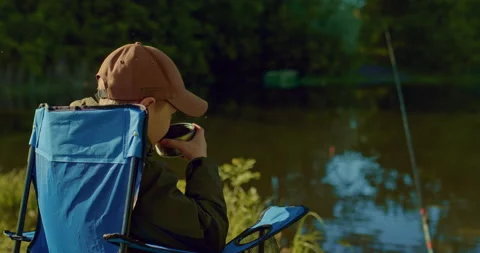 Little boy is resting and drinking tea when waiting bite, fishing rod in water 스톡 동영상 200717968
