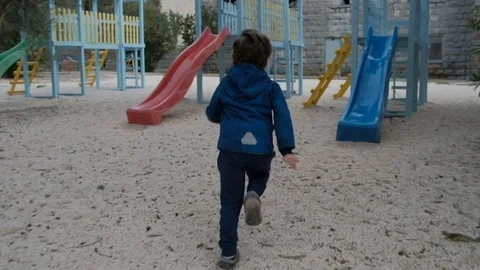 Little boy rides down a plastic slide on the playground in cool day Video stock 75788688