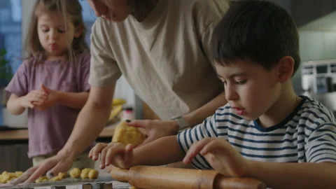 Little boy rolling dough while mother teaching little girl daughter pressing Stock Footage 265878854