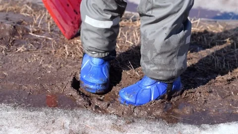 Little boy in rubber boots and waterproof pants is trampling in the spring mud. Stock Footage 152085408