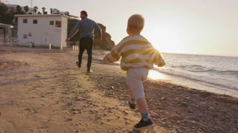 Little boy is running after his father, playing and smiling on beach at sunset Stock Footage 225536338
