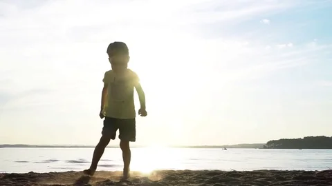 Little boy running on the beach kicking sand at sunset Stock Footage 78478549
