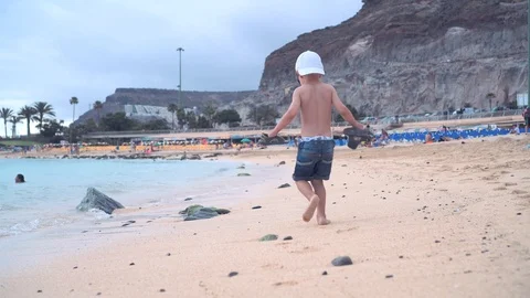 A little boy runs along the sandy beach along the coast and runs away from the Stock Footage 101756721