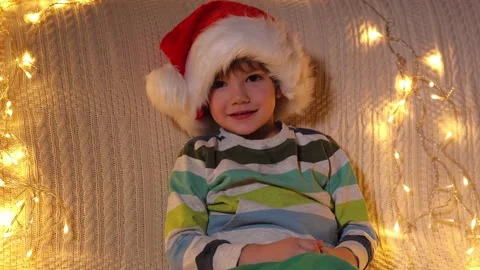 A little boy in a Santa hat is looking at the camera and smiling at holiday Stock Footage 164992600