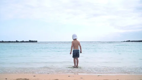 A little boy in shorts, a baseball cap and sunglasses is standing on a stone in Stock Footage 101758321