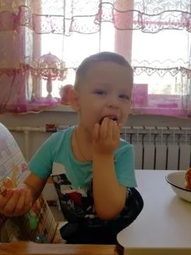 A little boy sits and eats a cake with his hands Stock Photos