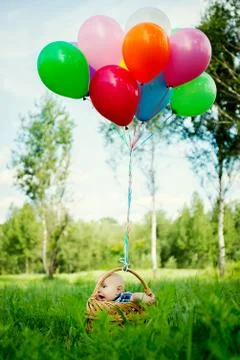 Little boy sits in a basket with colorful balloons Stock Photos