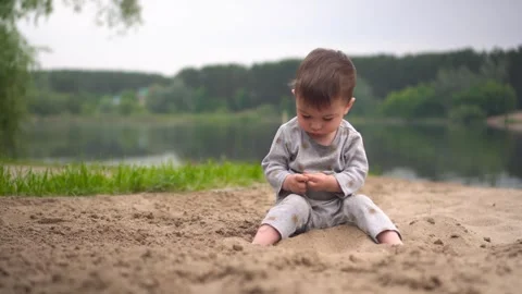 A little boy sits on the beach by the river and plays in the sand. A two-year Stock-Footage 246356660