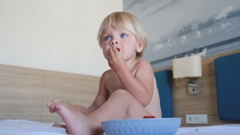 A little boy sits on a bed and eats strawberries Stock Footage 194777926