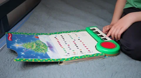 Little boy sits in bed, child playing Christmas Carol to a music book, keyboard Stock Footage 37389071