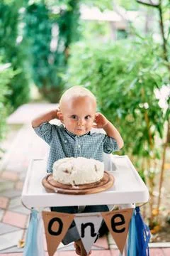 Little boy sits in front of a cake on the deck of his highchair Stock Photos