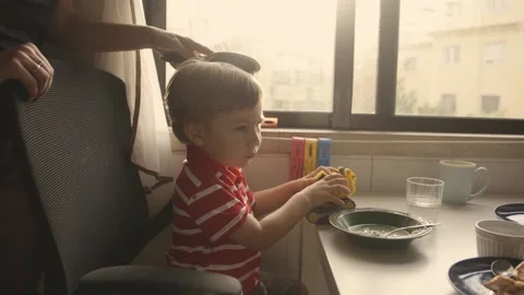 A little boy sits in the kitchen over a plate while his mother combs his hair Stock Footage 255041423