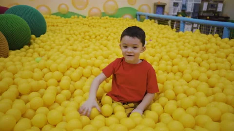 A little boy sits in a pool with balls and throws balls with his hand Video stock 169396005