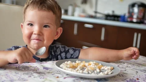 Little boy sits at the table, eats appetizing.The kid is good at using a spoon Stock Footage 153399821
