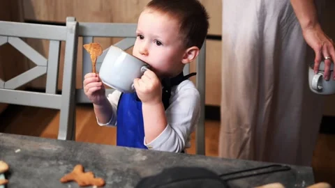 Little boy sits at table, one hand holding a mug of drink the other a cookie Vidéo 289518957