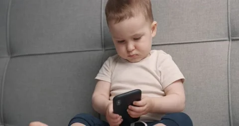 Little boy sitting on bed with mobile phone in hands and playing. Slow motion. Video stock 152565841