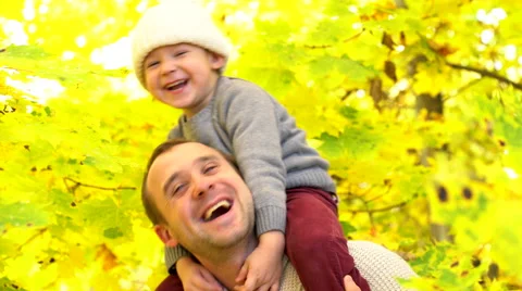 Little boy sitting in the neck of his father and gathering yellow maple leaves Stock Footage 68955182