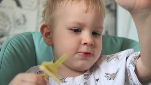 A little boy is sitting at a table and eating fruits: a banana and a pear Stock Footage 267539337