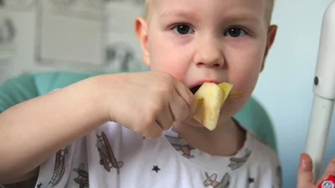 A little boy is sitting at a table and eating fruits: a banana and a pear Vidéo 267539419