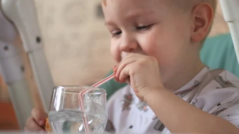 A little boy is sitting at a table, drinking water from a glass, from a tube Vidéo 267539236