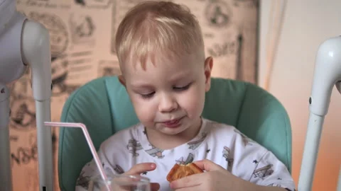 A little boy is sitting at a table, drinking water from a glass, from a tube Vidéo 267539269