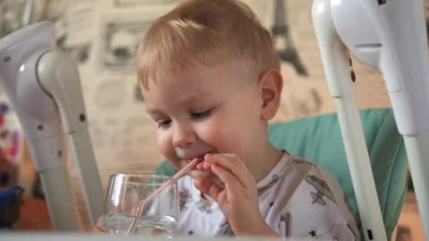 A little boy is sitting at a table, drinking water from a glass, from a tube Stock Footage 267539287