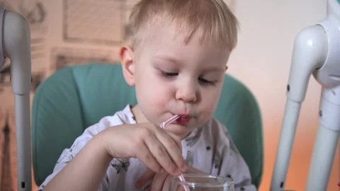 A little boy is sitting at a table, drinking water from a glass, from a tube Vidéo 267539574