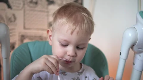 A little boy is sitting at a table, drinking water from a glass, from a tube Vidéo 267539659