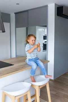 Little boy is sitting on a table in the kitchen and eating grapes. Stock Photos
