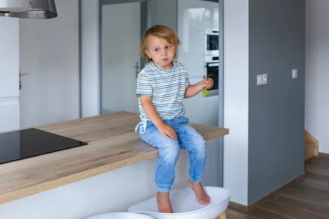 Little boy is sitting on a table in the kitchen and eating grapes. Stock Photos
