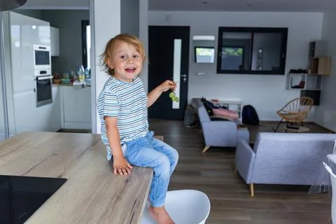 Little boy is sitting on a table in the kitchen and eating grapes. Stock Photos