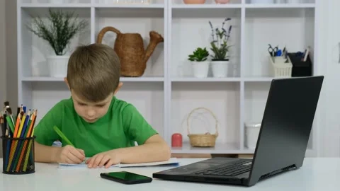 A little boy is sitting at a table in a room and doing homework Stockbeeldmateriaal 170844387