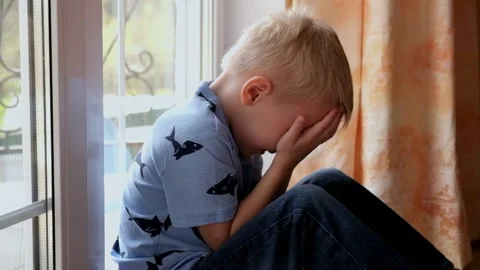 Little boy sitting at th window, hiding his face, feeling upset Stock Footage 89466861
