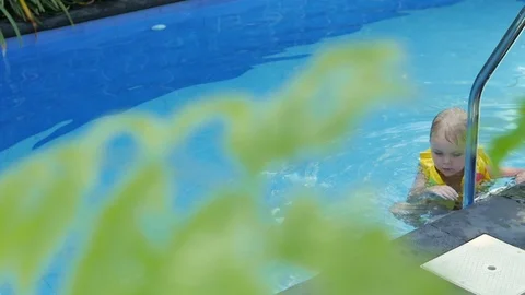 Little boy in sleeves and cap is swimming in the pool on vacation. boy swims in Видео 127149084