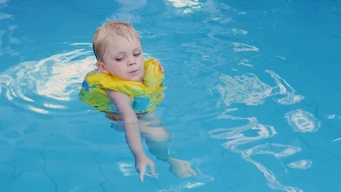 Little boy in sleeves and cap is swimming in the pool on vacation. boy swims in Stockbeeldmateriaal 128490732