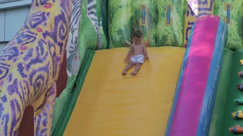 A little boy slides down a slide on a colorful trampoline platform Stock Footage 182327852