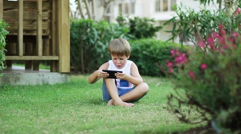 Little Boy With Smartphone Or Tablet Sitting In Garden On Green Grass. Stock Footage 56439699