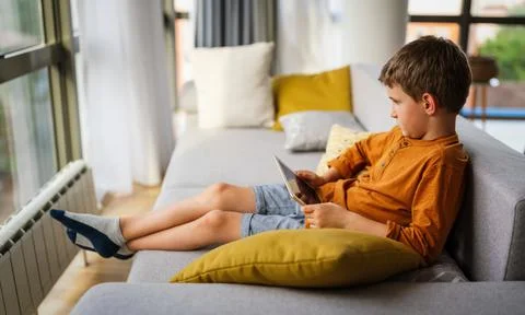 Little boy is smiling while playing or studying with digital tablet at home Stock Photos