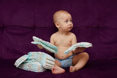 Little boy with stack of diapers or nappies on purple background Stock Photos