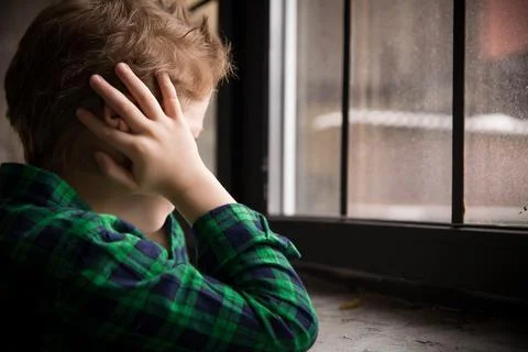 Little boy standing behind the window in sad mood. Sad Teenager looking in th Stock Photos
