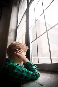 Little boy standing behind the window in sad mood. Sad Teenager looking in th Stock Photos