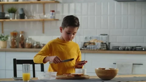 A little boy is standing in the kitchen making himself a blueberry jam Stock Footage 240059428