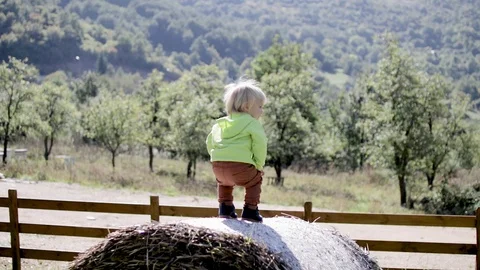A little boy stands and on a haystack against the backdrop of the mountains Stock Footage 128631076