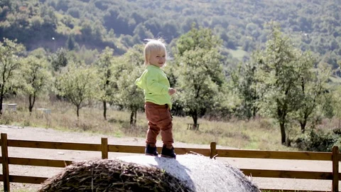 A little boy stands on a haystack against the backdrop of the mountains Video stock 128590356